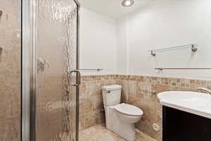 Bathroom featuring tile walls, vanity, an enclosed shower, toilet, and tile patterned floors