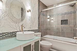 Full bathroom featuring vanity, shower / bath combination with glass door, toilet, and tasteful backsplash