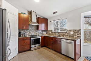 Kitchen with appliances with stainless steel finishes, sink, backsplash, plenty of natural light, and wall chimney range hood