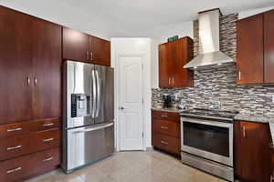 Kitchen with decorative backsplash, stainless steel appliances, wall chimney range hood, and light stone counters