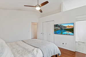 Bedroom with hardwood / wood-style flooring, a closet, connected bathroom, ceiling fan, and vaulted ceiling