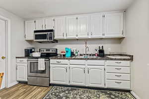 Kitchen featuring appliances with stainless steel finishes, light hardwood / wood-style flooring, sink, and white cabinets