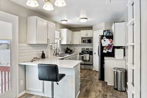 Kitchen with decorative backsplash, stainless steel appliances, white cabinetry, and wood-type flooring