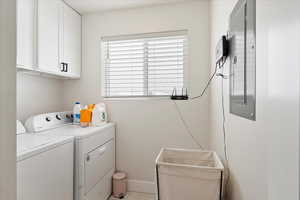 Laundry room with electric panel, washer and dryer, and cabinets