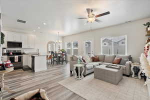 Living room with sink, light wood-type flooring, and ceiling fan with notable chandelier