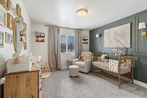 Carpeted bedroom featuring a crib and a textured ceiling