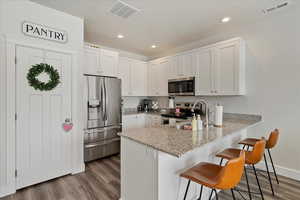 Kitchen with light wood-type flooring, appliances with stainless steel finishes, white cabinetry, and a kitchen breakfast bar