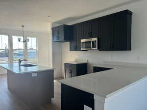 Kitchen with light hardwood / wood-style flooring, hanging light fixtures, an inviting chandelier, sink, and a kitchen island with sink