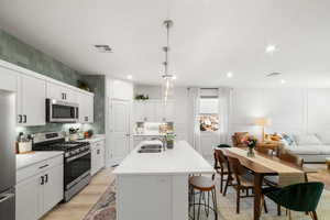 Kitchen with appliances with stainless steel finishes, white cabinets, decorative light fixtures, sink, and a kitchen island with sink