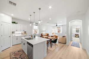 Kitchen featuring an island with sink, white cabinetry, sink, stainless steel dishwasher, and pendant lighting