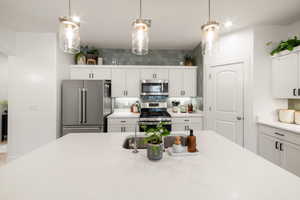 Kitchen featuring appliances with stainless steel finishes, decorative light fixtures, white cabinetry, and backsplash