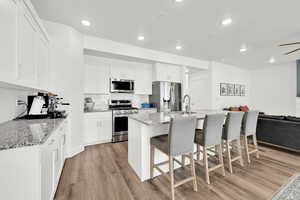 Kitchen with appliances with stainless steel finishes, a breakfast bar, light stone counters, white cabinetry, and an island with sink