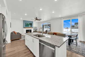 Kitchen featuring stainless steel appliances, light stone countertops, white cabinets, sink, and a kitchen island with sink