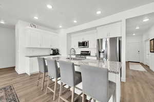 Kitchen with a kitchen island with sink, stainless steel appliances, light stone counters, white cabinets, and a kitchen bar