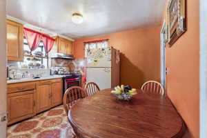 Kitchen with sink, stainless steel gas range oven, light tile patterned floors, white refrigerator, and decorative backsplash