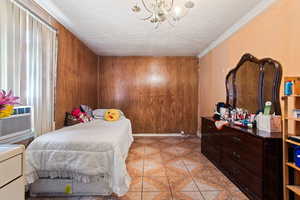 Tiled bedroom with an inviting chandelier, wooden walls, a textured ceiling, and crown molding