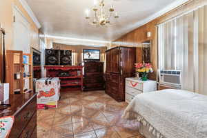 Tiled bedroom with cooling unit, crown molding, wooden walls, and a chandelier