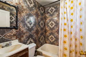 Full bathroom with vanity, tile walls, toilet, and shower / bathtub combination with curtain