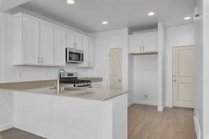 Kitchen with appliances with stainless steel finishes, light hardwood / wood-style floors, white cabinetry, and kitchen peninsula