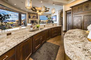 Kitchen with light stone counters, decorative light fixtures, a fireplace, sink, and dark hardwood / wood-style floors