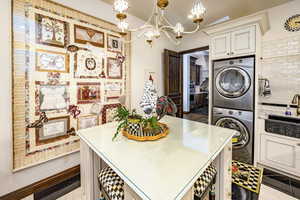 Kitchen featuring cream cabinets, hanging light fixtures, tasteful backsplash, stacked washing maching and dryer, and a chandelier