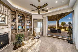 Living area featuring a tray ceiling, a brick fireplace, carpet, and ceiling fan