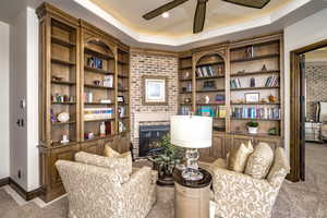 Living area with a tray ceiling, built in shelves, carpet flooring, and a fireplace