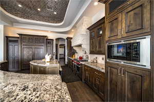 Kitchen with a center island, stainless steel appliances, dark wood-type flooring, a raised ceiling, and light stone countertops