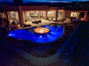 Pool at twilight with a patio, an outdoor living space with a fire pit, and pool water feature