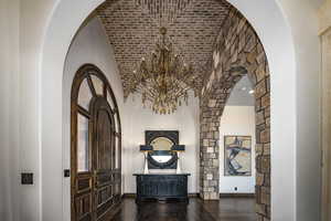 Entrance foyer featuring a chandelier, dark hardwood / wood flooring, and a high ceiling with brick detail and beautiful arched grand entry door.