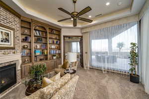 Sitting room featuring a raised ceiling, ceiling fan, carpet flooring, and a fireplace