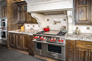 Kitchen with stainless steel appliances, light stone countertops, dark brown cabinets, custom exhaust hood, and decorative backsplash