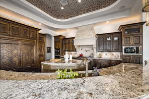 Kitchen with built in appliances, brick ceiling, custom range hood, a raised ceiling, and dark brown cabinetry