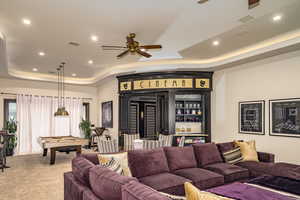 Living room with indoor bar, ceiling fan, billiards, light carpet, and a tray ceiling