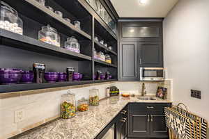 Bar featuring sink, beverage cooler, light stone counters, and tasteful backsplash