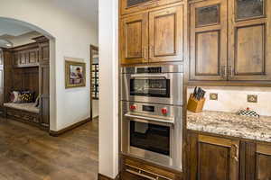 Kitchen featuring stainless steel double oven, decorative backsplash, dark hardwood / wood-style floors, and light stone countertops