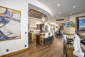 Kitchen with premium range hood, light stone countertops with island, decorative light fixtures, and a sweeping curved kitchen bar