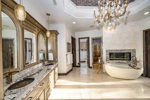 Bathroom with a chandelier, vanity, a washtub, a tray ceiling, and a high end fireplace