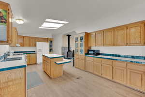 Kitchen with white refrigerator with ice dispenser, sink, light hardwood / wood-style flooring, a center island, and a wood stove