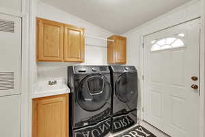 Clothes washing area featuring washer and dryer, cabinets, crown molding, and a textured ceiling