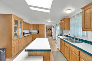 Kitchen featuring light hardwood / wood-style flooring, dishwasher, a kitchen island, sink, and lofted ceiling with skylight