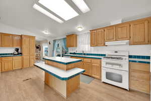 Kitchen with sink, light wood-type flooring, white gas range oven, and a center island