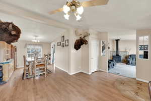 Dining area with ceiling fan with notable chandelier, light hardwood / wood-style flooring, vaulted ceiling with beams, and a wood stove