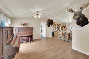 Sitting room featuring ceiling fan with notable chandelier, light wood-type flooring, and lofted ceiling with beams