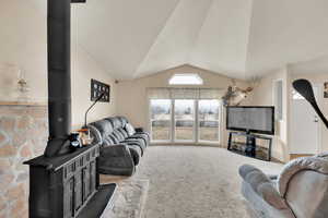 Living room with a wood stove, carpet flooring, and lofted ceiling