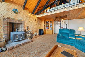 Carpeted living room with a wood stove, beam ceiling, wooden ceiling, wooden walls, and rail lighting