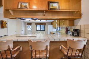 Kitchen featuring white fridge, sink, a kitchen breakfast bar, kitchen peninsula, and tile counters