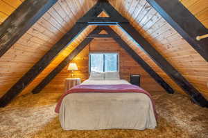 Carpeted bedroom with wood walls, lofted ceiling with beams, and wood ceiling