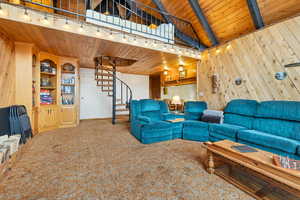 Carpeted living room with wood walls, rail lighting, wood ceiling, and lofted ceiling with beams