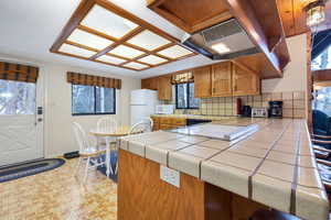 Kitchen featuring exhaust hood, white appliances, tile counters, and backsplash